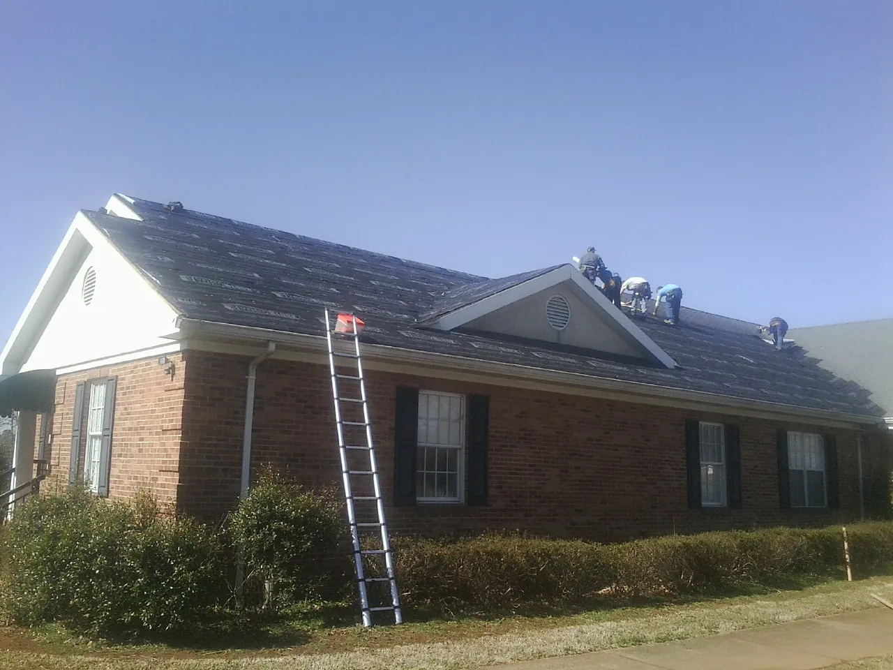 Crew tearing shingles off a brick ranch roof with a ladder set — Emergency Roof Repair work by our crew in Edwards