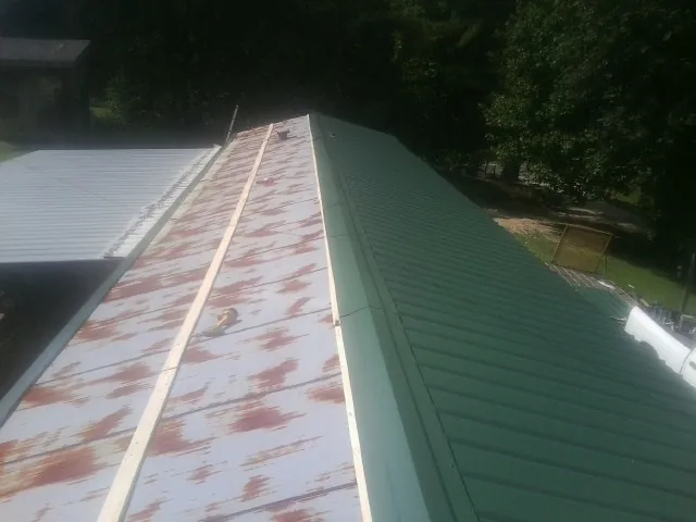 Old rusted panels beside newly installed green metal roofing — Wind Damage Roof Repair by Roofing Brothers in Edwards